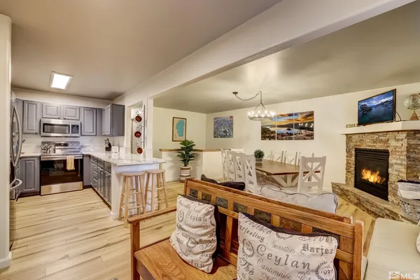 a living room with stainless steel appliances furniture a fireplace a flat screen tv and a kitchen view