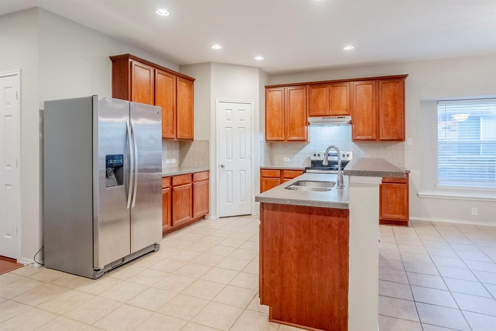 1113 Mount Olive Lane Forney, TX 75126 - Photo 13 of 39 Kitchen featuring stainless steel fridge with ice dispenser, backsplash, brown cabinets, light tile patterned flooring, and a kitchen island with sink
