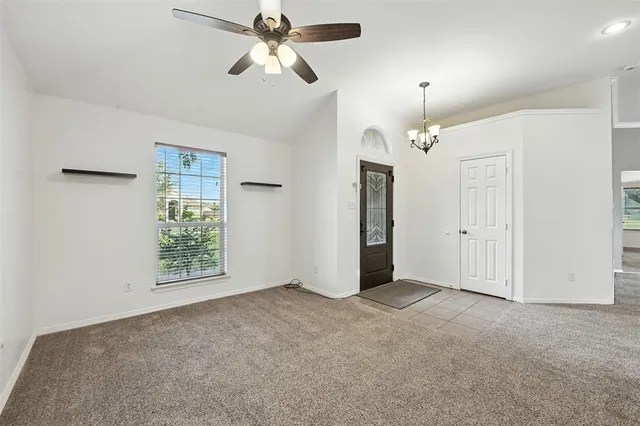 an empty room with chandelier fan and windows