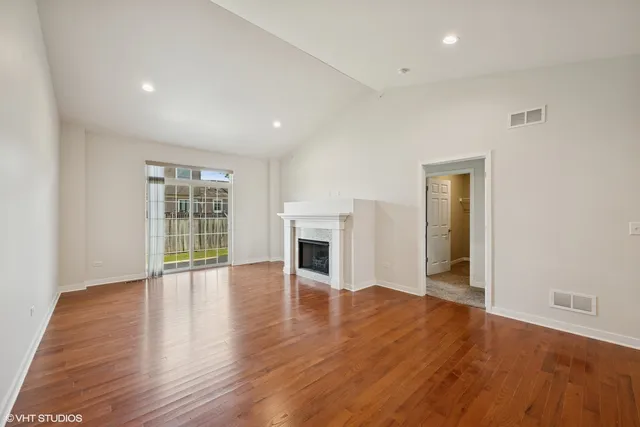 an empty room with wooden floor fireplace and windows