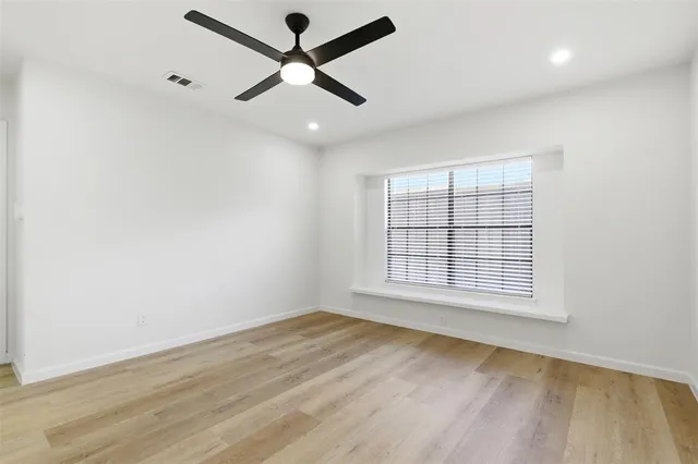 an empty room with wooden floor ceiling fan and windows