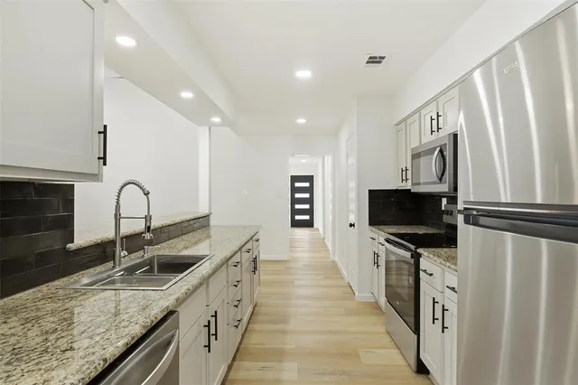 a kitchen with stainless steel appliances granite countertop a sink and a stove top oven with wooden floor