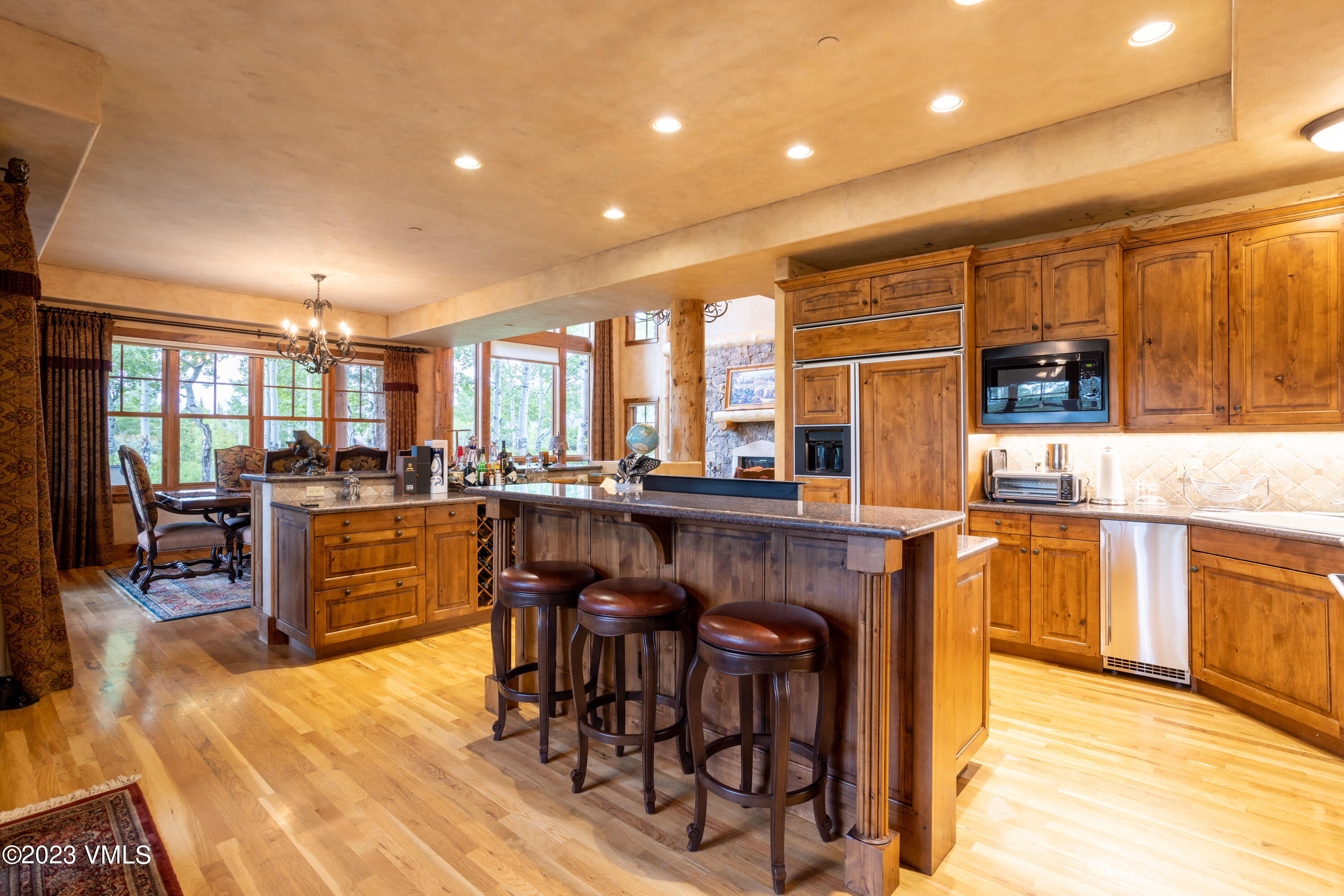a kitchen with stainless steel appliances kitchen island granite countertop a refrigerator a stove top oven and a dining table with wooden floor
