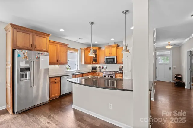 a kitchen with stainless steel appliances granite countertop a refrigerator a sink dishwasher a stove and a dining table with wooden floor