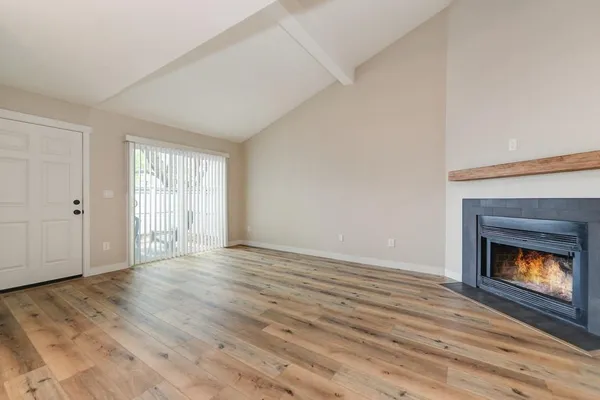 a view of an empty room with wooden floor fireplace and a window