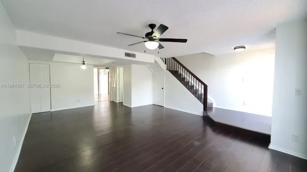 a view of an empty room with wooden floor and a ceiling fan