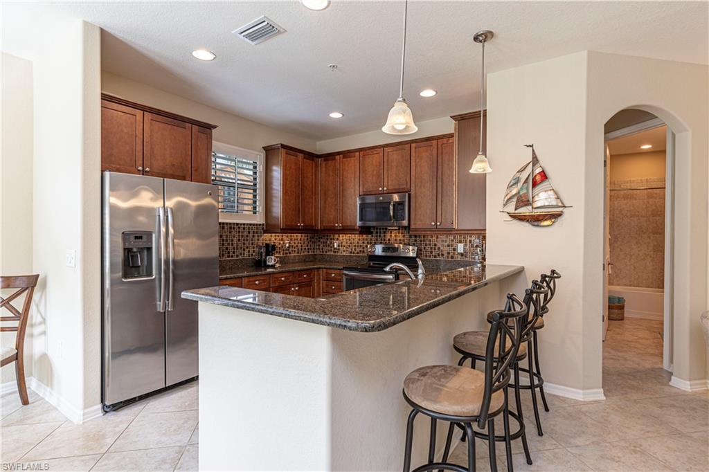 9063 Capistrano Street North, Unit 4405 Naples, FL 34113 - Photo 7 of 37 a kitchen with stainless steel appliances granite countertop a sink a stove a refrigerator a microwave oven with a dining table and chairs