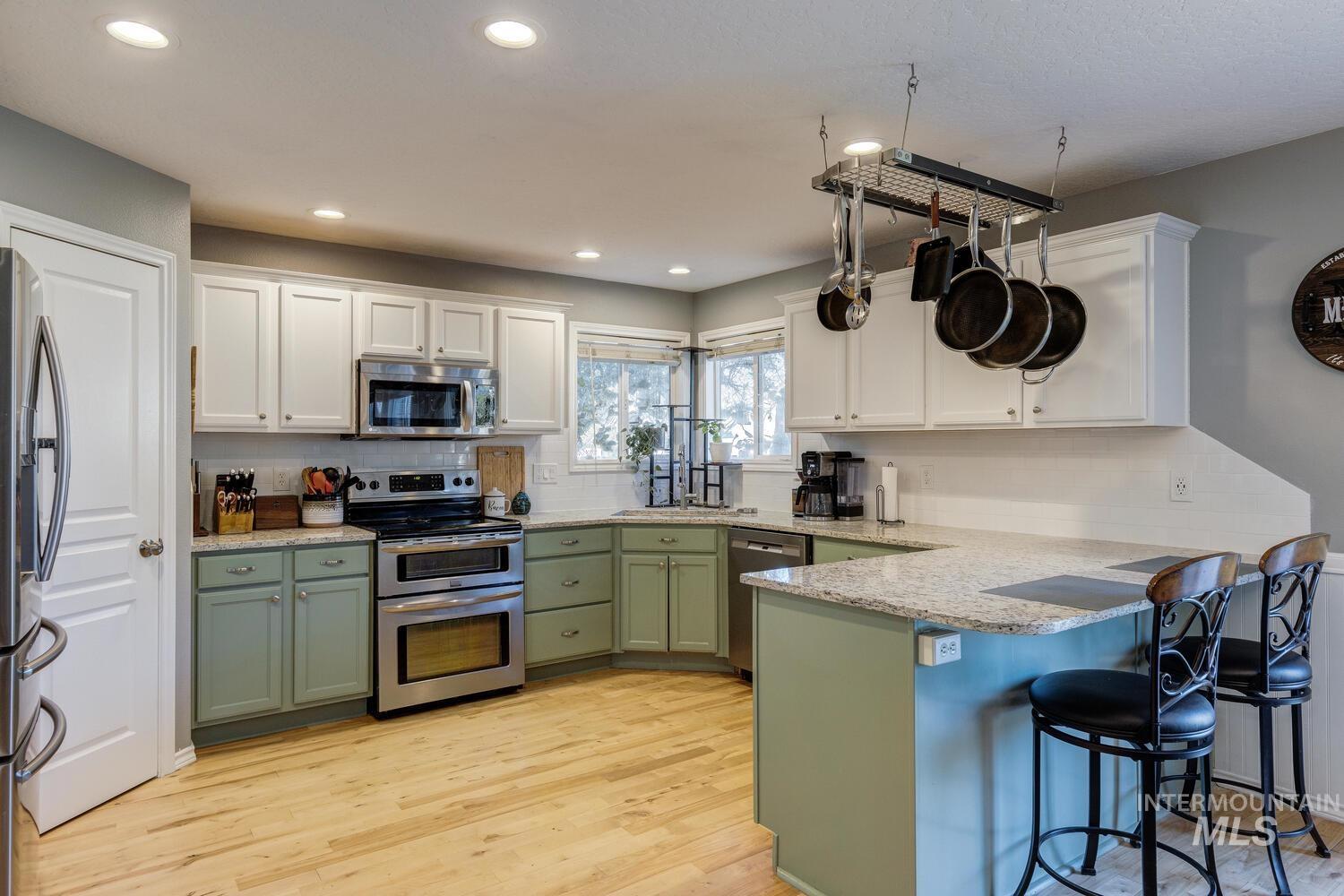 4428 West Campfire Street Meridian, ID 83646 - Photo 14 of 46 Kitchen featuring green cabinets, white cabinets, appliances with stainless steel finishes, light wood-style flooring, and recessed lighting