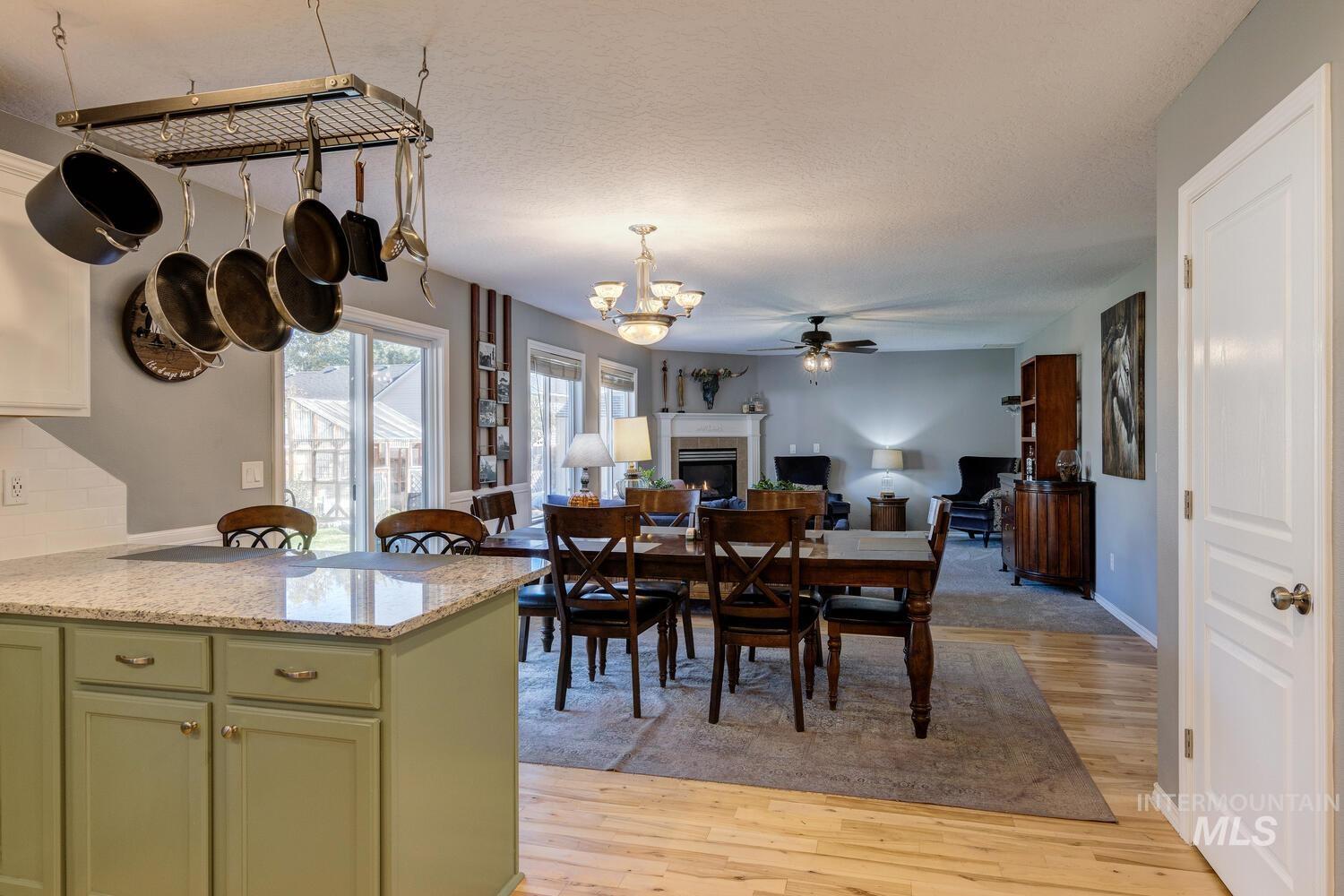 4428 West Campfire Street Meridian, ID 83646 - Photo 17 of 46 Dining space with a warm lit fireplace, light wood-type flooring, a ceiling fan, a chandelier, and a textured ceiling