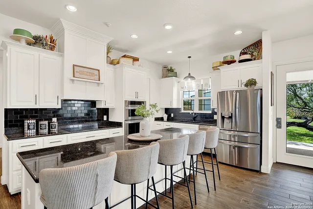 a kitchen with stainless steel appliances granite countertop a refrigerator a stove a sink dishwasher and a dining table with wooden floor