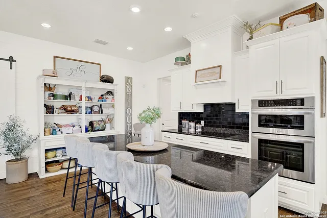 a kitchen with stainless steel appliances granite countertop a stove top oven a sink dishwasher and a dining table with wooden floor