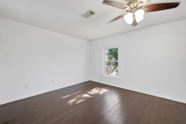 an empty room with wooden floor chandelier fan and windows