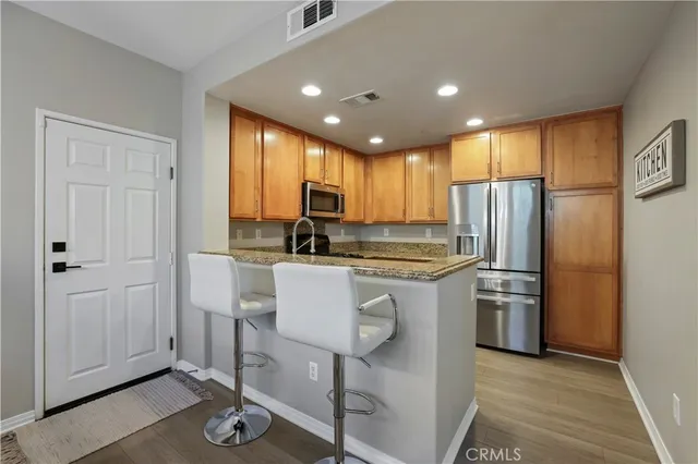 a kitchen with stainless steel appliances granite countertop a refrigerator a stove and a sink with wooden floor