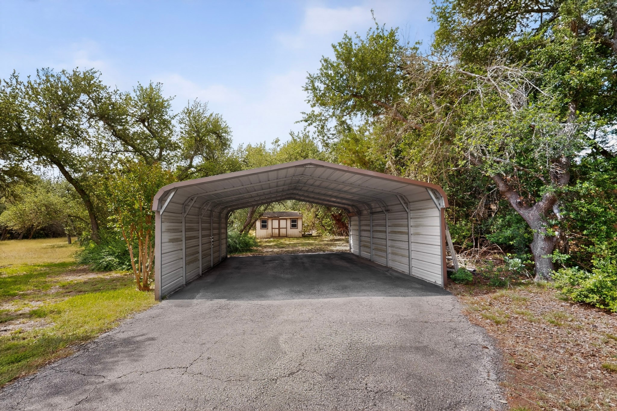 1003 Pier Branch Road Dripping Springs, TX 78620 - Photo 37 of 40 A dedicated carport offers protected parking, with a quaint shed nestled amongst natural landscaping.