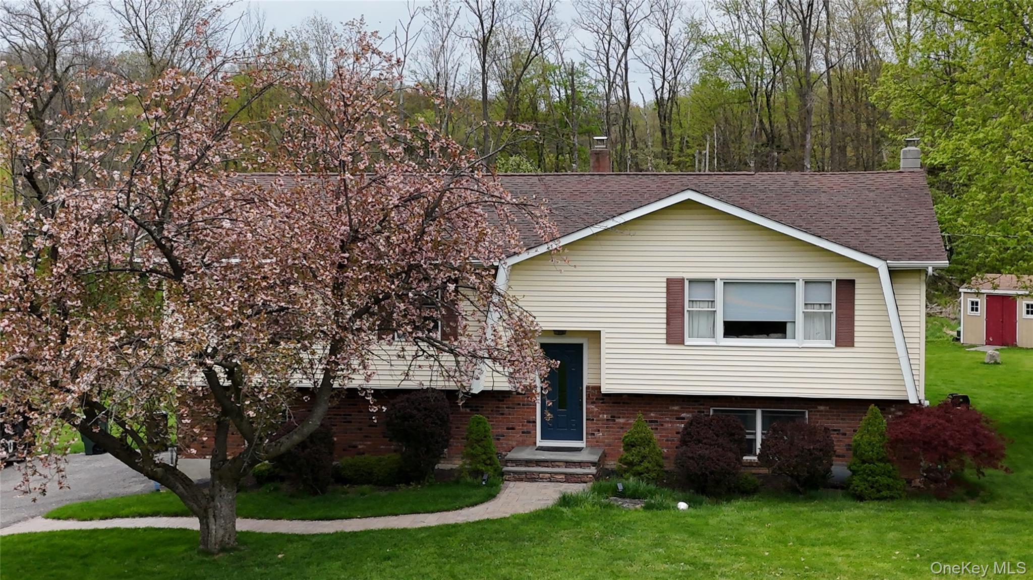 Split-level residence featuring a brick and siding exterior The front elevation features a gambrel style slice view roof line, a prominent flowering tree, and a neatly manicured lawn