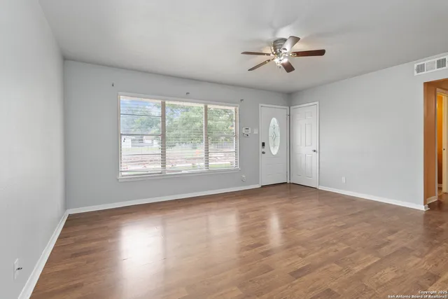 an empty room with wooden floor chandelier fan and windows