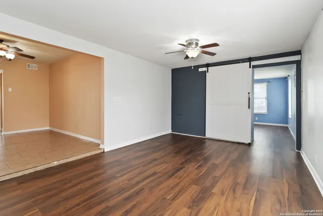 a view of an empty room with wooden floor and a ceiling fan