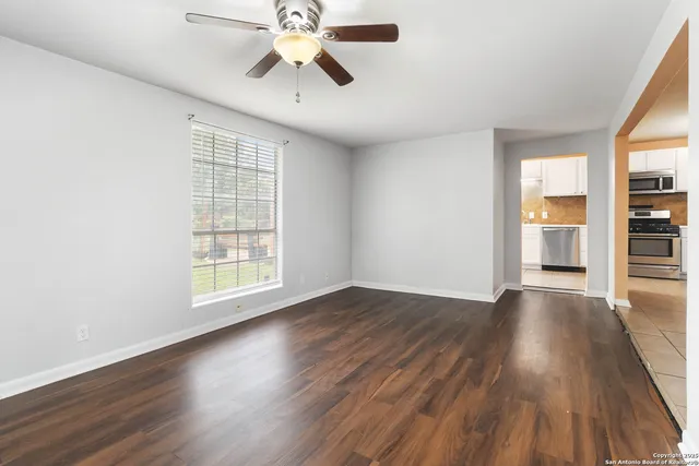an empty room with wooden floor chandelier fan and windows