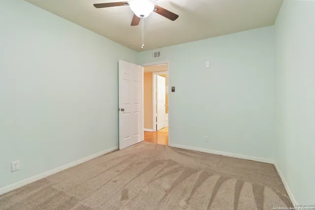 an empty room with a chandelier fan and wooden floor