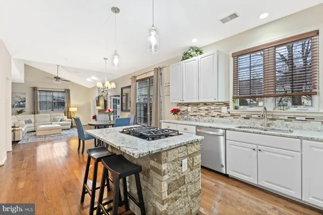 a kitchen with stainless steel appliances kitchen island granite countertop a stove a sink dishwasher and white cabinets with wooden floor