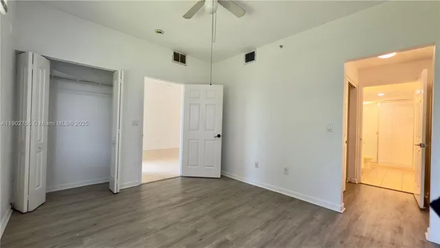a view of an empty room with wooden floor and a ceiling fan