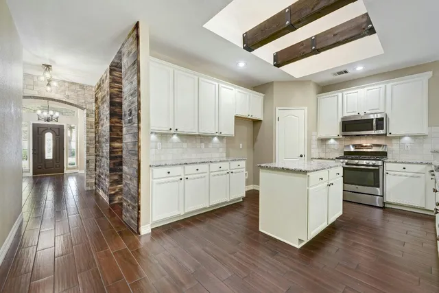 a kitchen with stainless steel appliances kitchen island granite countertop a stove a sink and white cabinets with wooden floor
