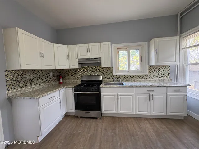 a kitchen with granite countertop a refrigerator a stove top oven and wooden floor