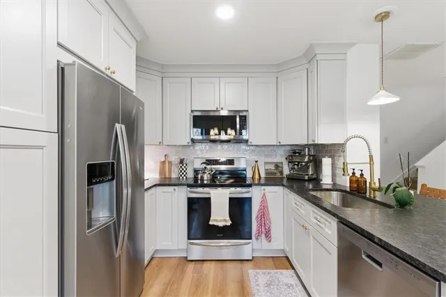 a kitchen with stainless steel appliances granite countertop a refrigerator a stove a sink and white cabinets