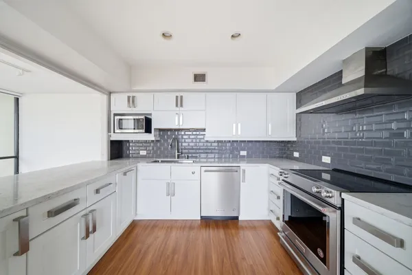 a kitchen with stainless steel appliances granite countertop a stove top oven a sink dishwasher and white cabinets with wooden floor