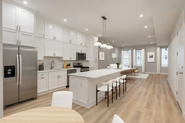 a large white kitchen with lots of counter space dining table and stainless steel appliances