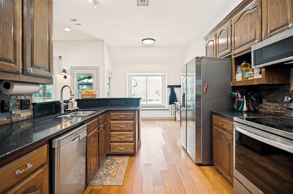5643 West Caylor Road Fort Worth, TX 76244 - Photo 13 of 37 Kitchen featuring wood-finish flooring, dark wood cabinetry, and stainless steel appliances including a refrigerator, dishwasher, and microwave