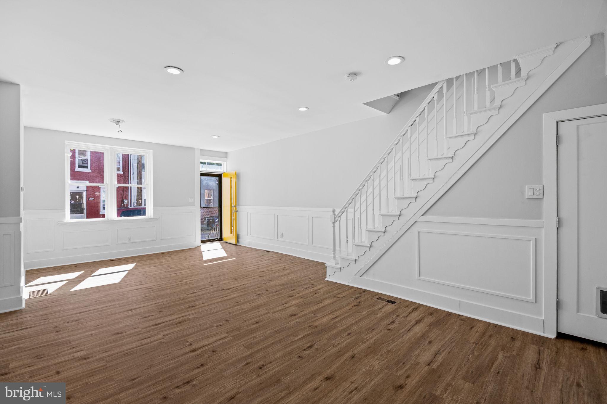 a view of an empty room with wooden floor and stairs