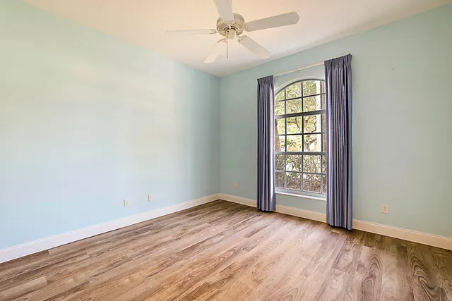 an empty room with wooden floor chandelier fan and windows