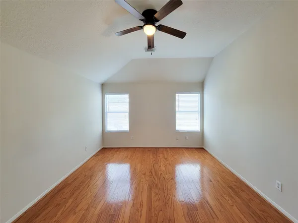 an empty room with wooden floor ceiling fan and windows