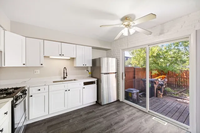 a kitchen with stainless steel appliances granite countertop a stove a refrigerator a sink and white cabinets with wooden floor