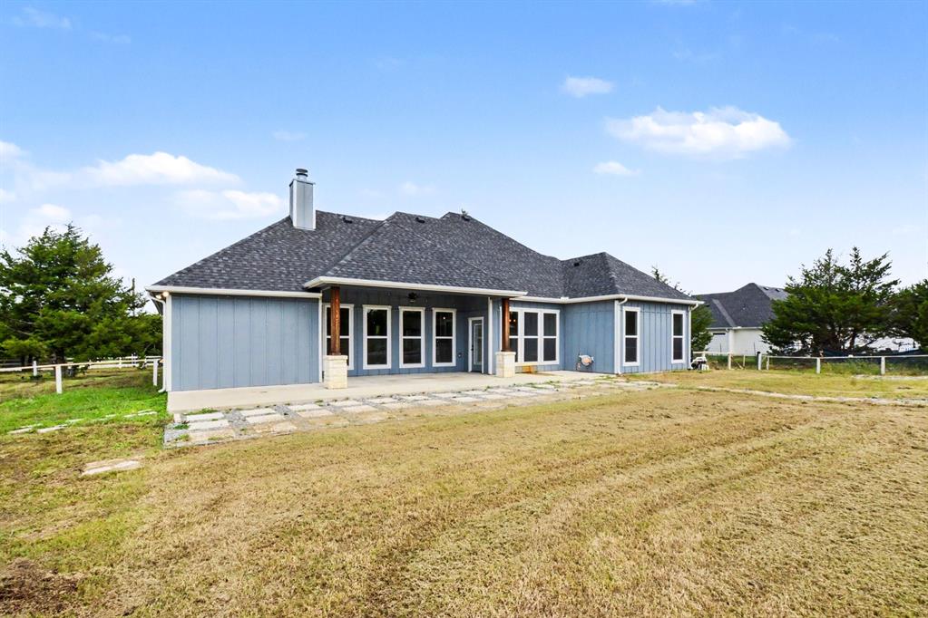 530 P R 491 Leonard, TX 75452 - Photo 34 of 35 Rear exterior featuring blue vertical siding, a dark shingle roof, multiple windows, and a stone patio