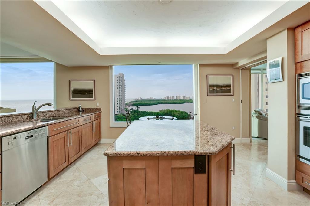 20 Seagate Drive, Unit 803 Naples, FL 34103 - Photo 12 of 40 Kitchen featuring light stone countertops, stainless steel appliances, a kitchen island, wood finish cabinetry, and a tray ceiling