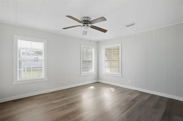 an empty room with wooden floor fan and windows
