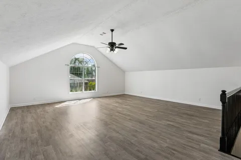 an empty room with wooden floor chandelier fan and windows