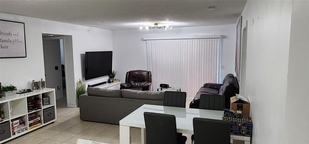 5005 Wiles Road, Unit 106 Coconut Creek, FL 33073 - Photo 6 of 19 a living room with furniture a chandelier and a flat screen tv