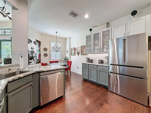 a kitchen with stainless steel appliances granite countertop a refrigerator a sink dishwasher a stove and white cabinets with wooden floor