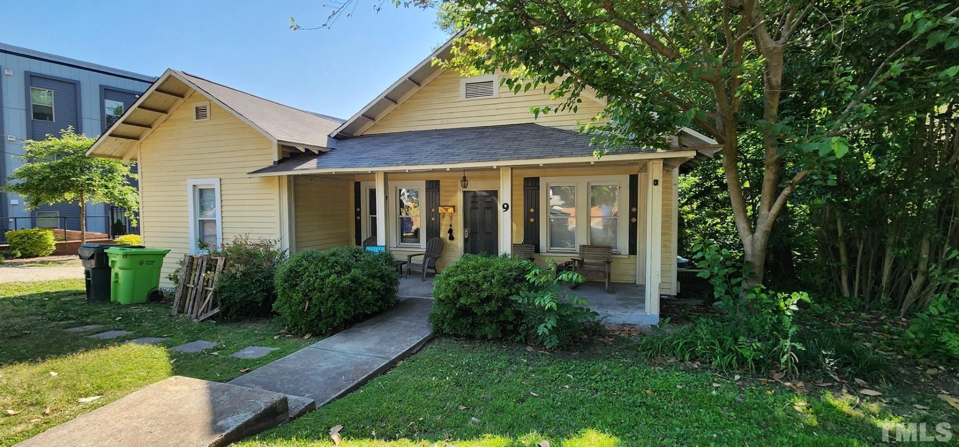 a view of a brick house with a yard plants and large tree