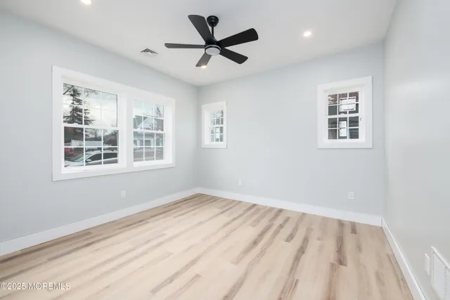 a view of empty room with wooden floor and fan