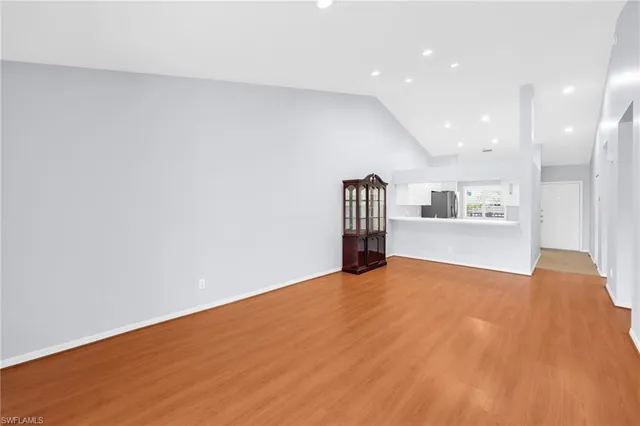 a view of an empty room with wooden floor and a kitchen