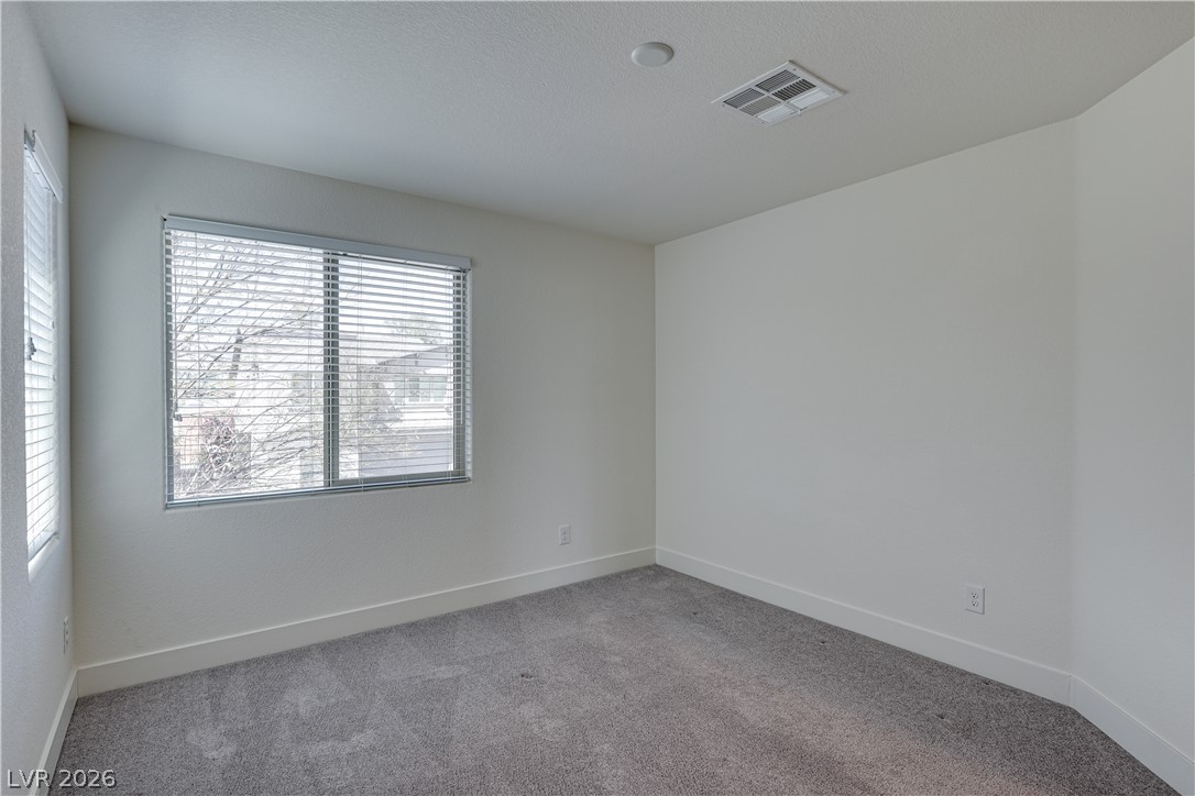 5954 Smith Valley Road Las Vegas, NV 89148 - Photo 18 of 23 A well-lit bedroom features plush gray carpeting and a wide window offering natural illumination.