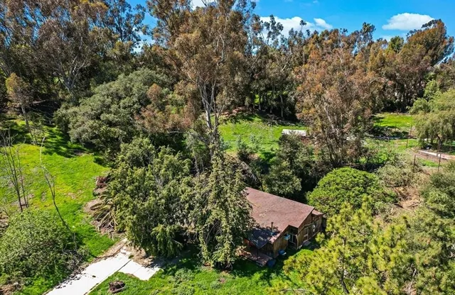 an aerial view of a residential houses with outdoor space and trees all around
