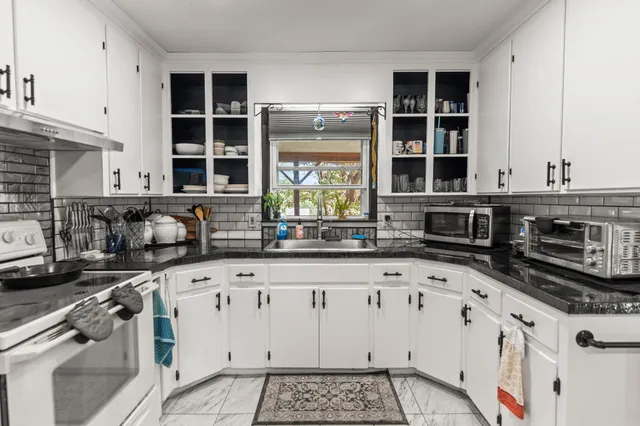 a kitchen with granite countertop a stove a sink and a white cabinets