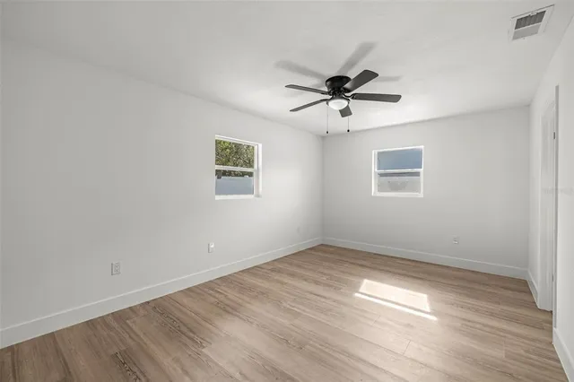 an empty room with wooden floor ceiling fan and windows