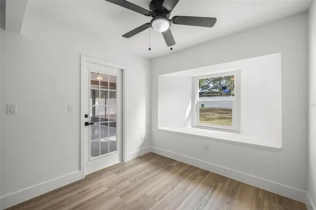 an empty room with wooden floor chandelier fan and windows