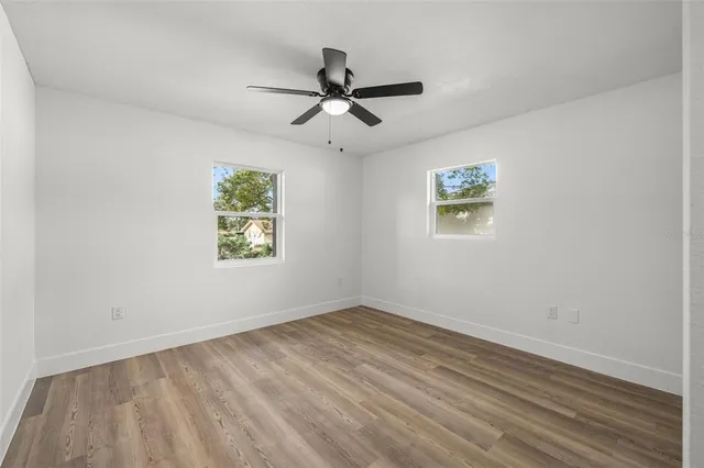 an empty room with wooden floor ceiling fan and windows